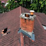 Brick chimney and surrounding shingled roof showing combined weather damage at the flashing line — Spring Hill Chimney Service NEPA